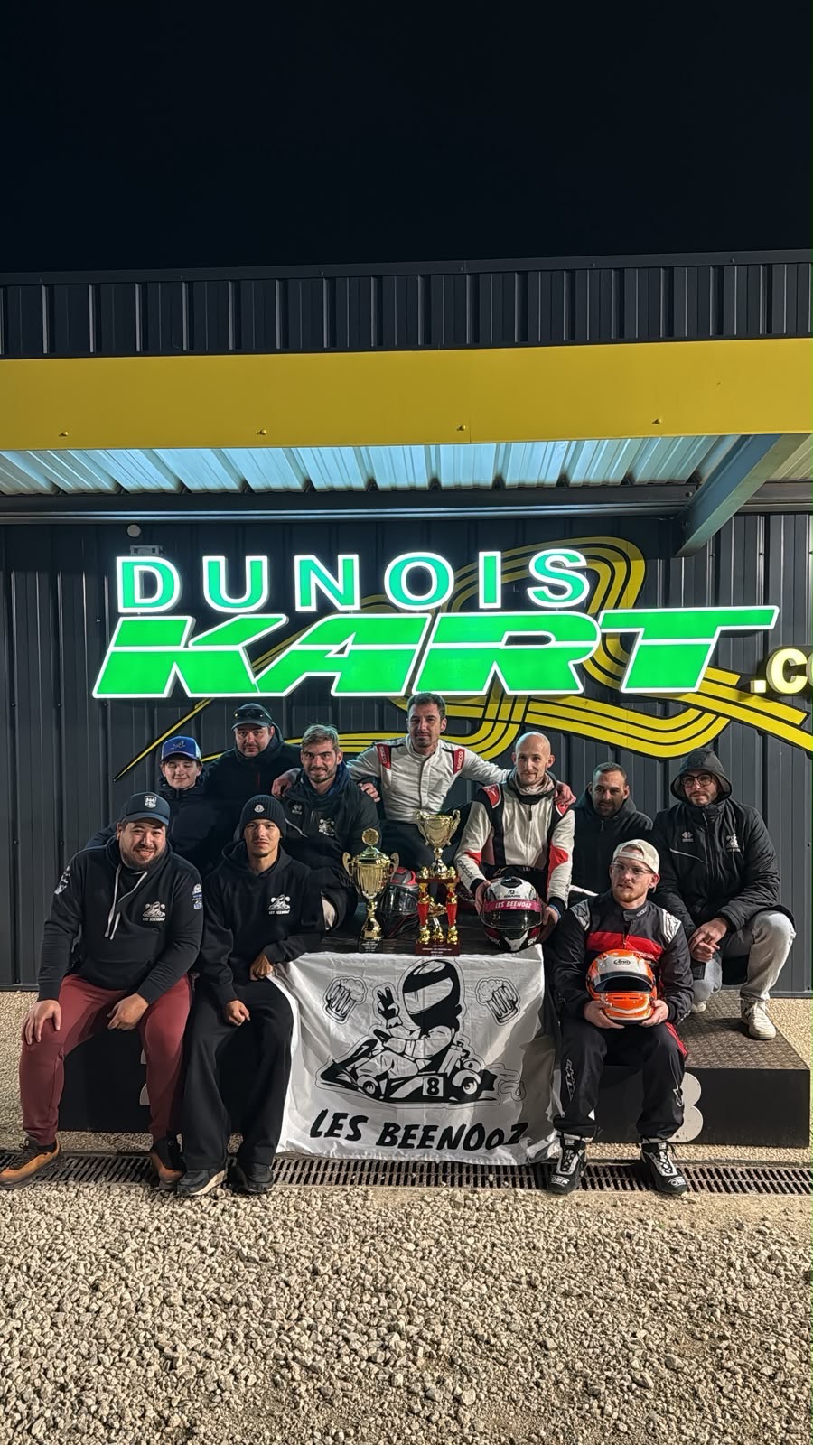 L'équipe des Beenooz réunie de nuit devant le Dunois Kart avec deux trophées et le drapeau du club, après les 12 h